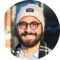 Portrait of a man with a beard wearing a white beanie and glasses. He appears to be enjoying a city trip.
