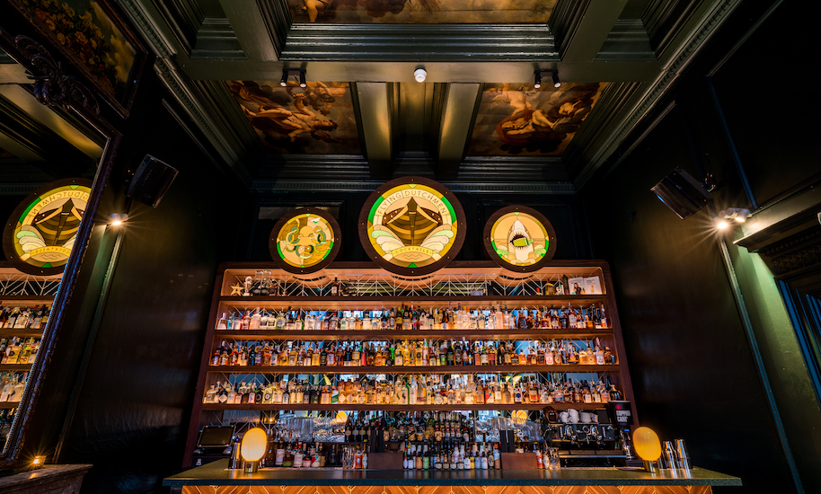 Il bancone scuro del Flying Dutchman cocktail bar di Amsterdam con una parete piena di bottiglie per miscelare ottimi cocktail.