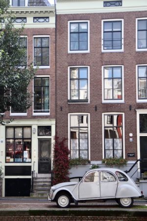 A classic white car parked on a street in Amsterdam. The car is in front of a traditional Dutch building.