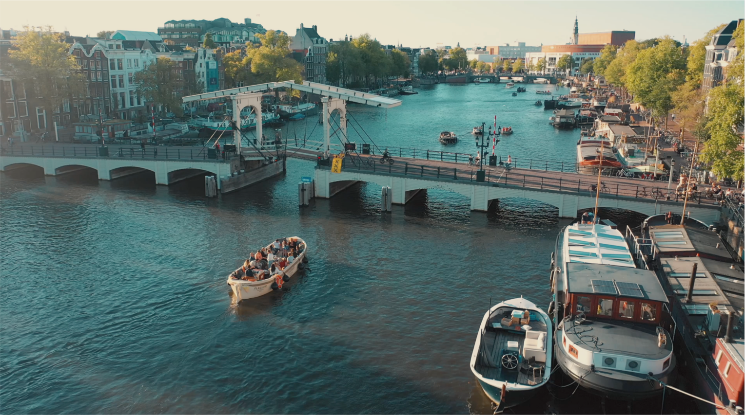 A scenic view of Amsterdam canals with boats and bridges. A tourist boat sails through the waterway.