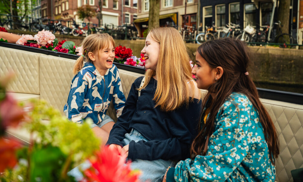Three young women on a boat trip in Amsterdam. They are smiling and enjoying the city view.